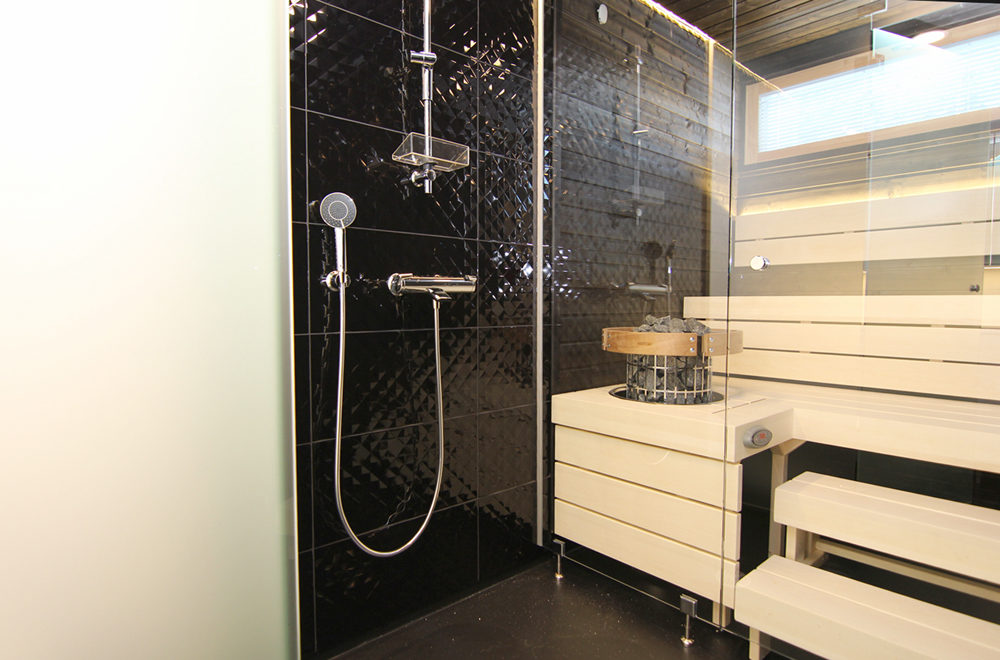 Kylpyhuoneen musta laatoitettu tehosteseinä jatkuu myös saunassa.