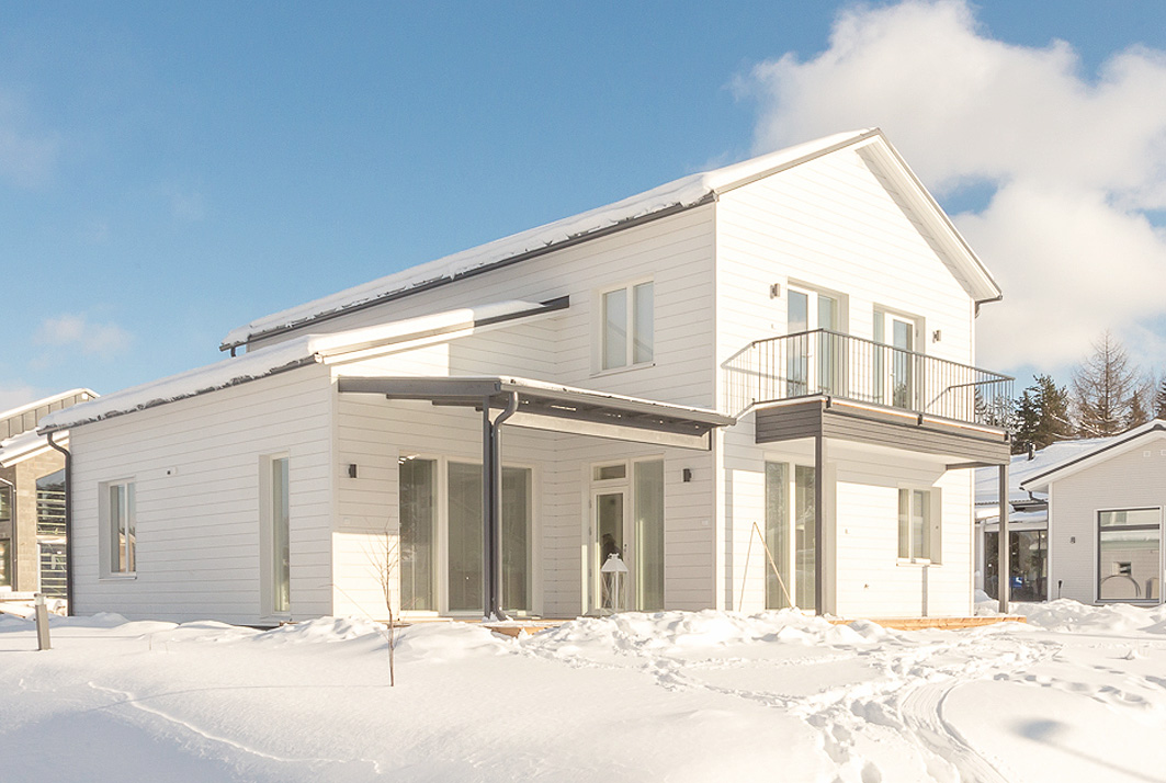 Omakotitalon rakentaminen - valkoisen talon pihalla on runsaasti lunta ja aurinko paistaa kirkkaasti.