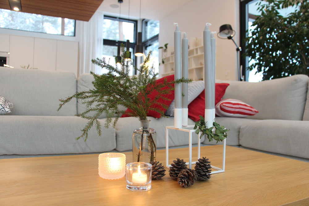 Hiljennymme joulun viettoon. Sohvapöydällä on tuikkukynttilöitä, kynttilän jalka ja käpyjä.